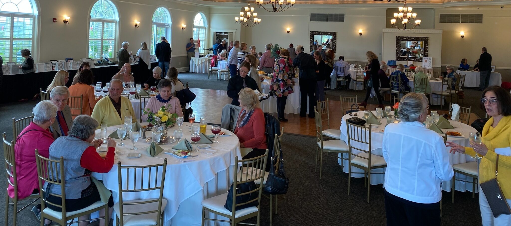 Groups of people at tables and talking at a cocktail party.